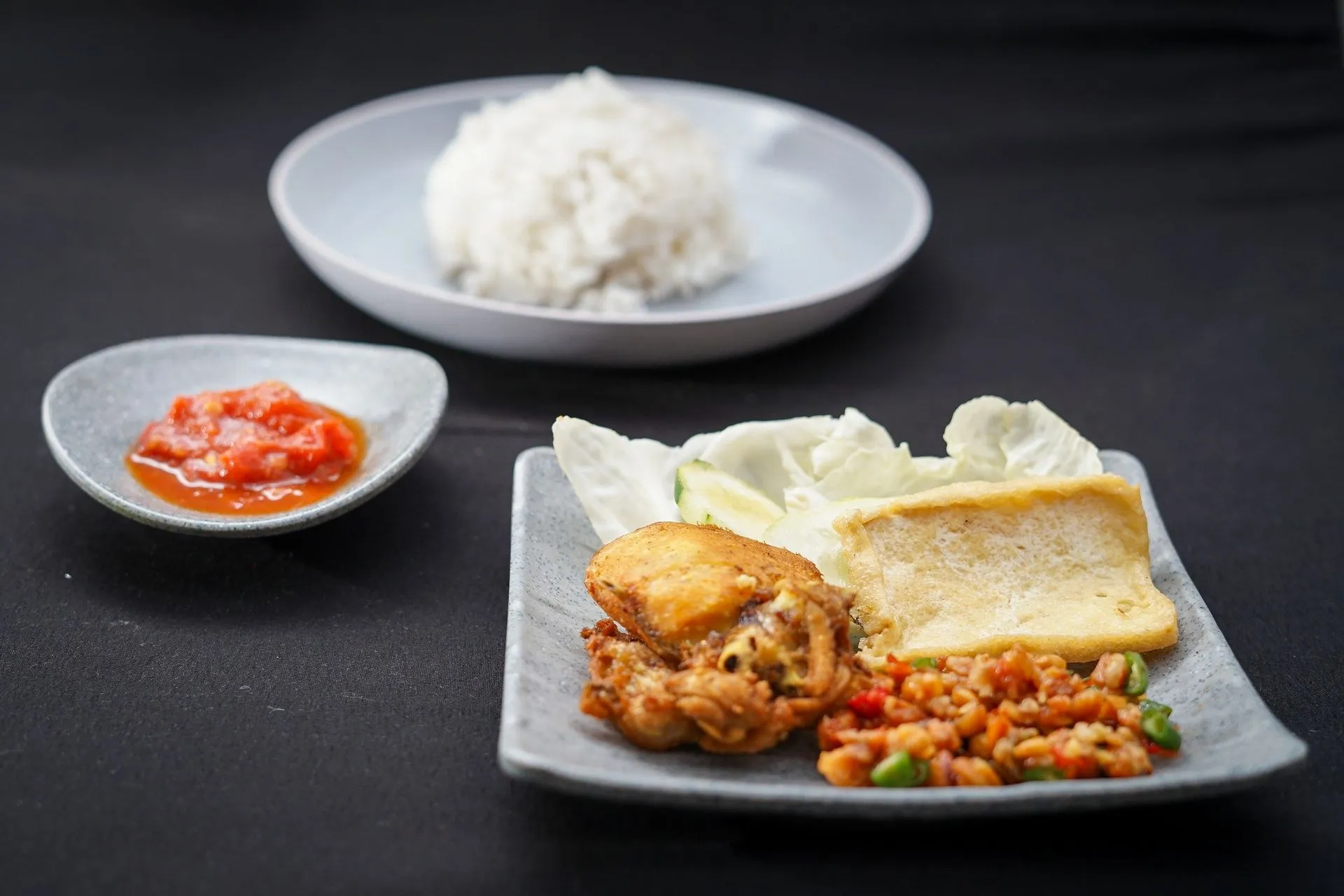 Nasi putih dengan ayam goreng, tahu, dan sambal di piring saji